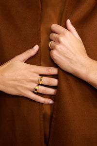 Woman in a rust-coloured coat wearing gold plated rings from Carré. The two rings on the right are Signét rings, one set with a labradorite gemstone, and the left ring is a fishbone ring