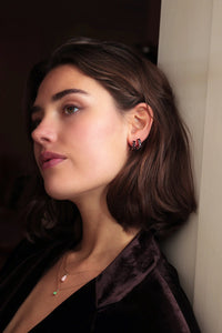 Smiling woman wearing gold plated sterling silver jewellery from Carré. The long earrings are set with January's birthstone garnet. The ear stud is also set with a red garnet gemstone.