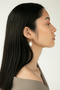 Woman standing sideways wearing a twist gold plated hoop from Carré, and a charm with a large freshwater pearl.