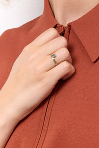 Woman in a rust shirt wearing a 10-karat solid gold ring from Carré set with a blue gemstone. The gemstone is a london blue topaz, which is november's birthstone