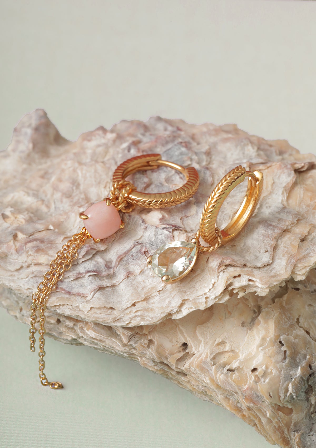 Two gold plated hoops from Carré in creole style set with charms. The charms have a pink opal gemstone, a chain charm, and a prasiolite charm.