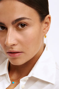 Woman wearing 10-karat gold jewellery from Carré. The earring is set with a golden champagne quarts, and a long ear stud with a chain set with london blue topaz