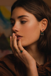 Woman wearing a long gold plated earring from Carré. The earring is set with green agate which is may's birthstone.