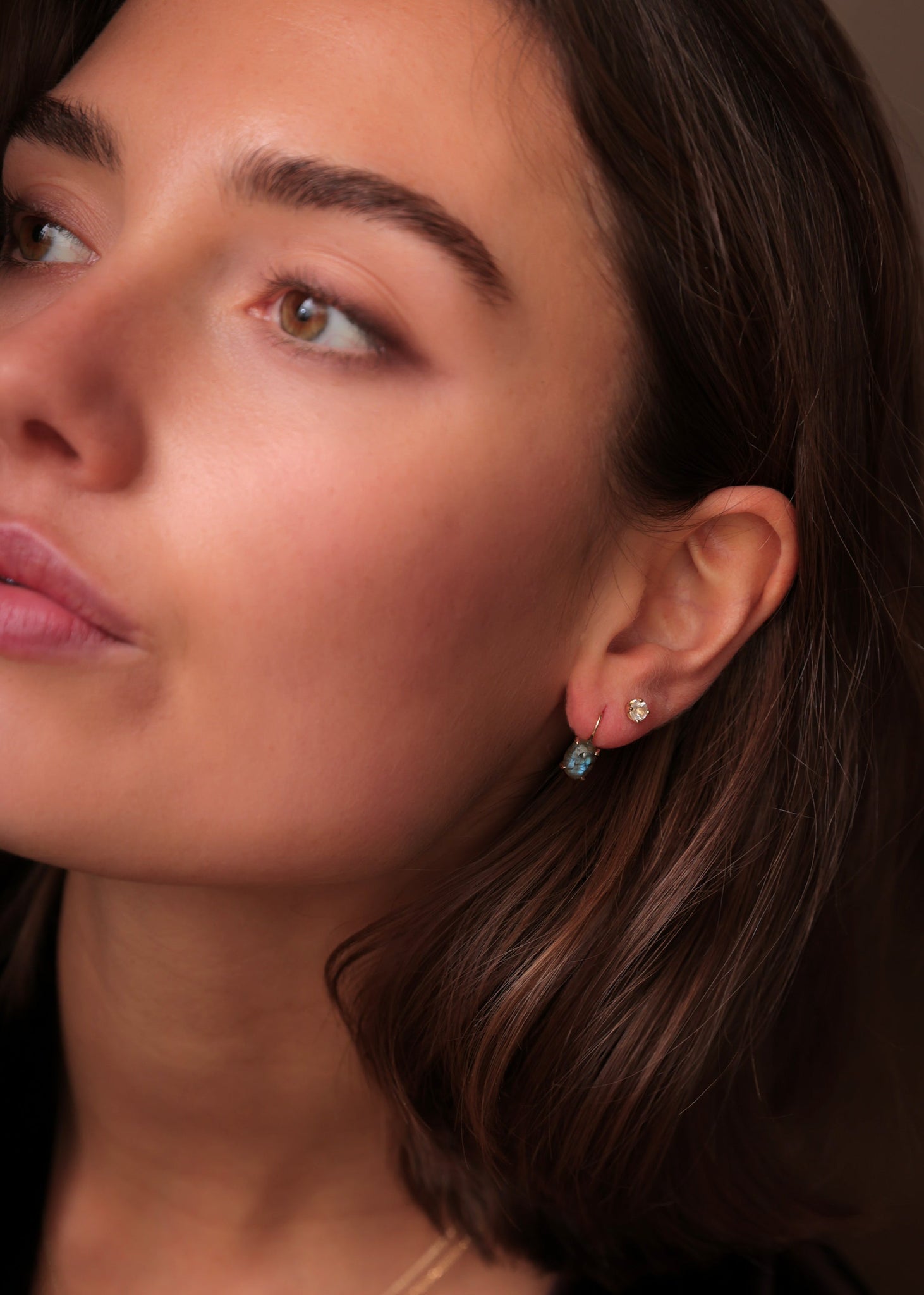 Woman wearing gold plated long earrings from Carré. The long earrings have a chain and are set with three labradorite gemstones