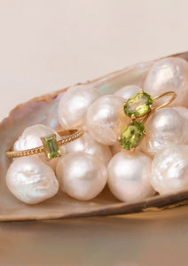 Gold plated jewellery from Carré laying on a bed of pearls. The jewellery is set with a green gemstone, Peridot