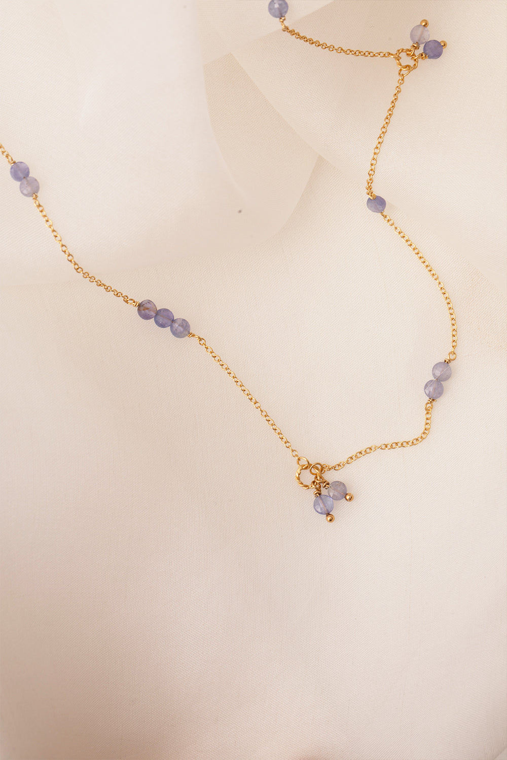 Smiling woman wearing a gold plated long earring from Carré set with three rows of the purple gemstone tanzanite