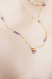Smiling woman wearing a gold plated long earring from Carré set with three rows of the purple gemstone tanzanite