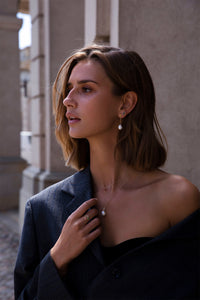 woman with solid gold jewellery from carré. She wears a pearl necklace and long pearl earrings and an ear stud with green tourmaline