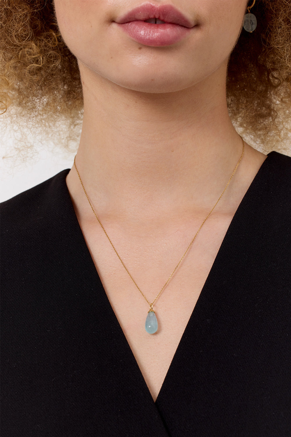 woman wearing a gold necklace and pendant from carré. The pendant is a large aquamarine pendant for necklaces