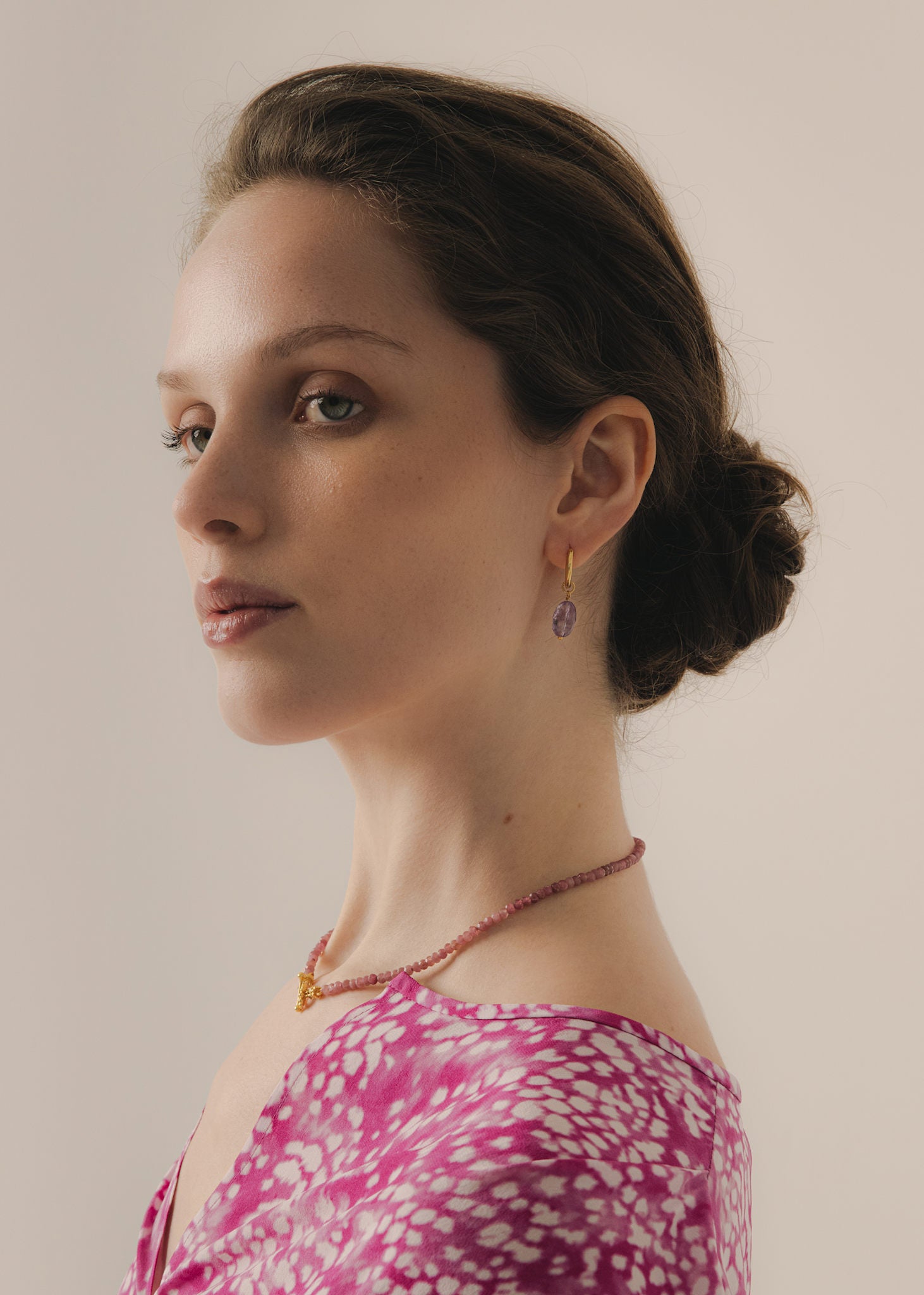 Woman wearing large amethyst charm earrings on golden hoops for office use