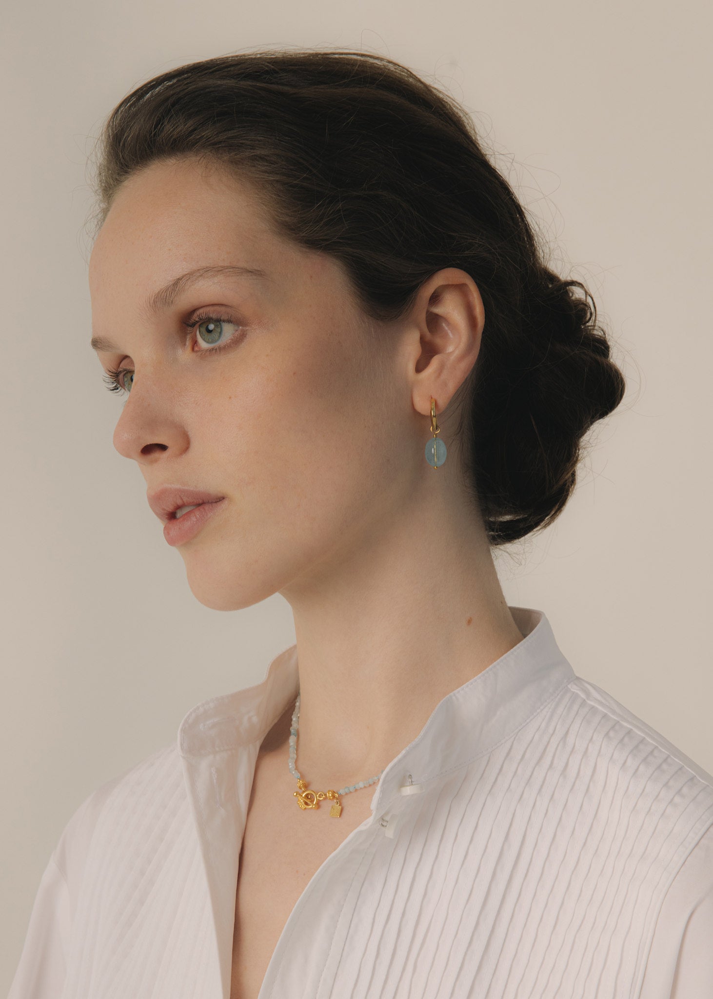 Woman wearing large blue aquamarine earring hoops in gold with a beaded aquamarine necklace for wedding day jewellery