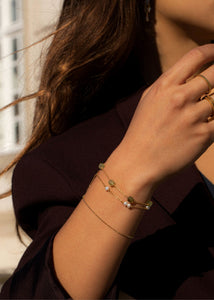Kvinde med guldbelagte armbånd med ægte ædelsten og tynde kæder fra carré jewellery med grønne granater og ferskvandsperler