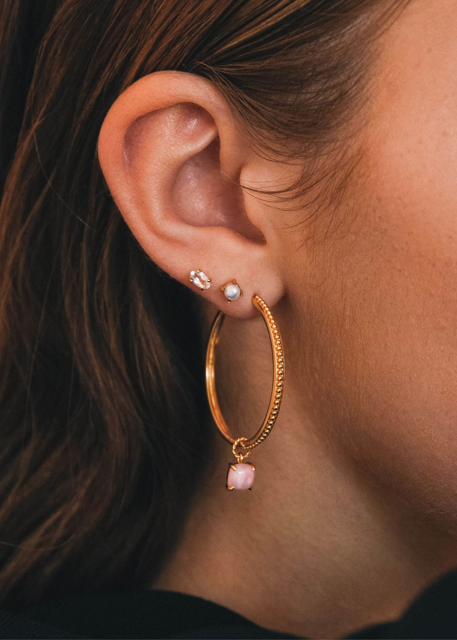 Kvinde med store hoop øreringe i guld og et charm til øreringe med lyserød opal ædelsten fra carré jewellery's hoops og charms sortiment 