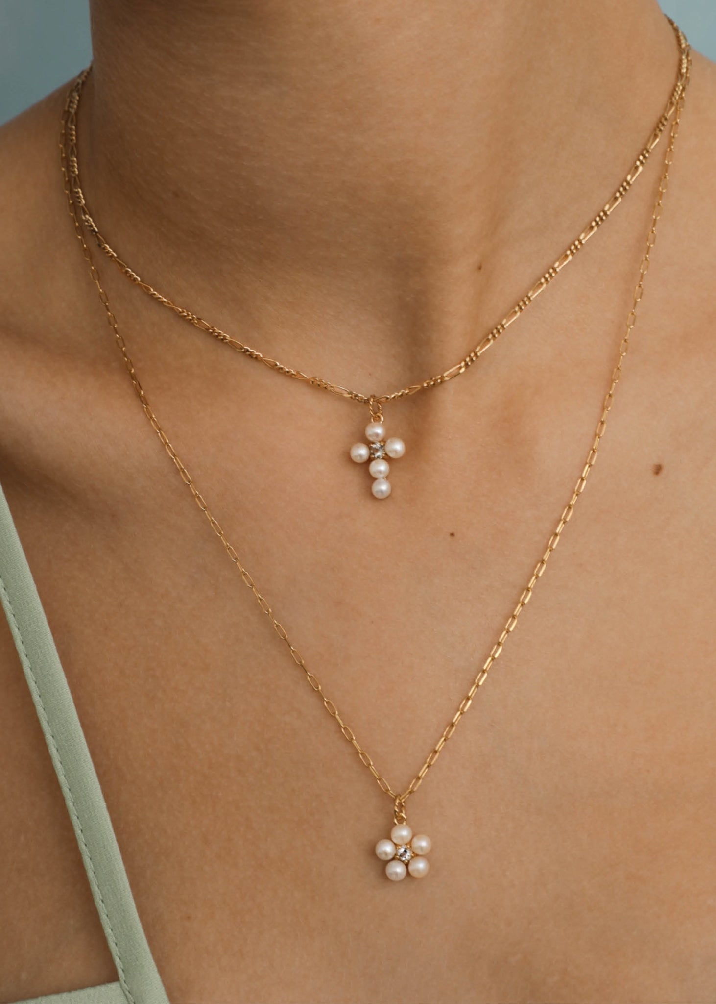 Woman wearing two pendants for necklaces in gold in a cross shape and one in a flower shape