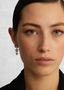 Woman wearing long dangling pearl earrings from carré jewellery in a flower shape with white freshwater pearls in gold plated sterling silver