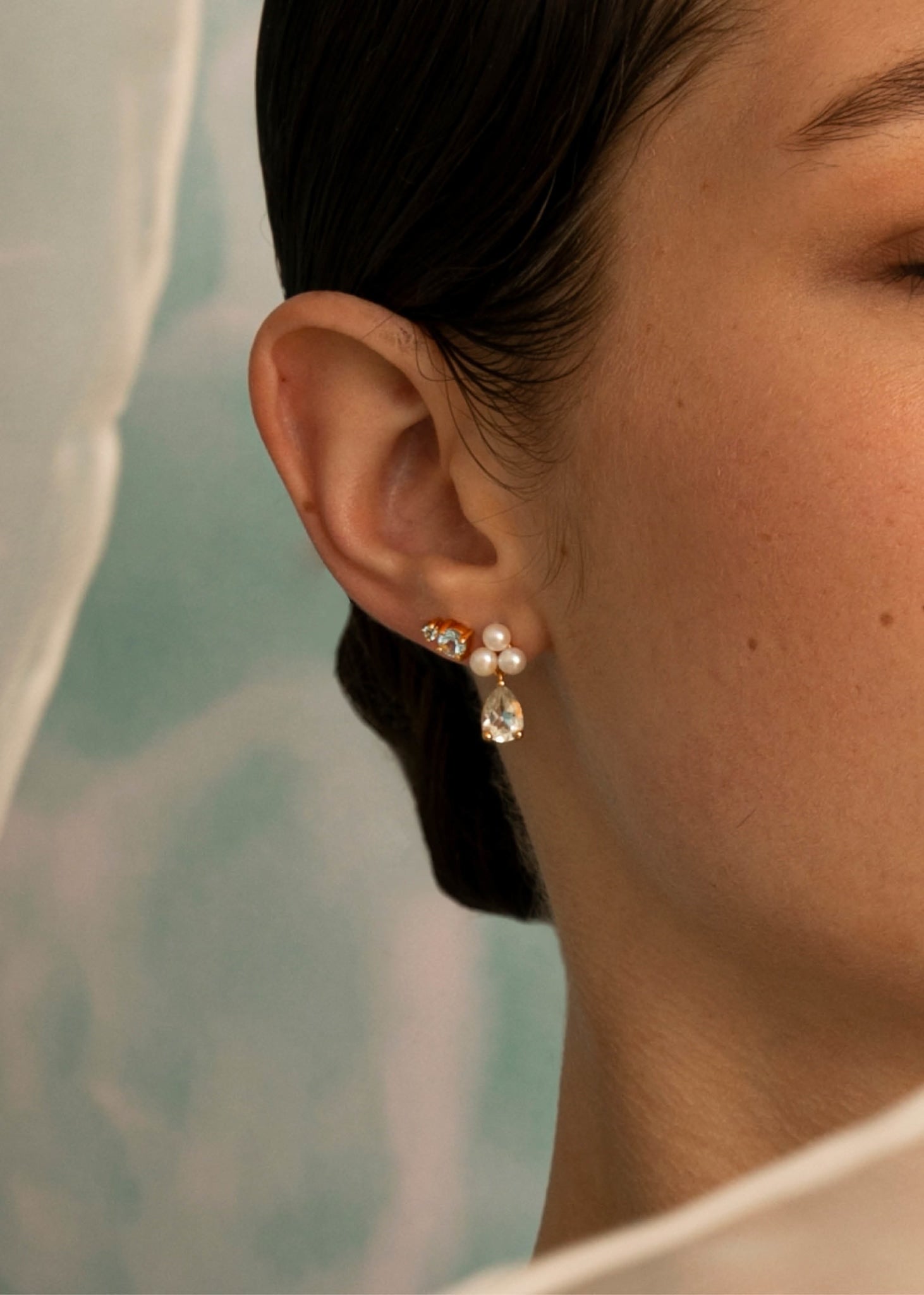 Bride wearing gold plated ear studs from carré jewellery set with three round white freshwater pearls and a drop of pear cut prasiolite gemstone