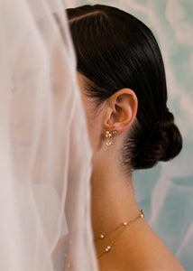 Bride wearing gold plated ear studs from carré jewellery set with three round white freshwater pearls and a drop of pear cut prasiolite gemstone