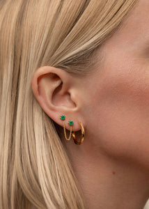 Woman with a double ear stud set with two facet-cut green emerald gemstones