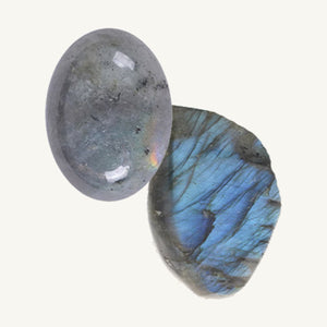 a cabochon-cut Labradorite and a raw labradorite gemstone on a beige background