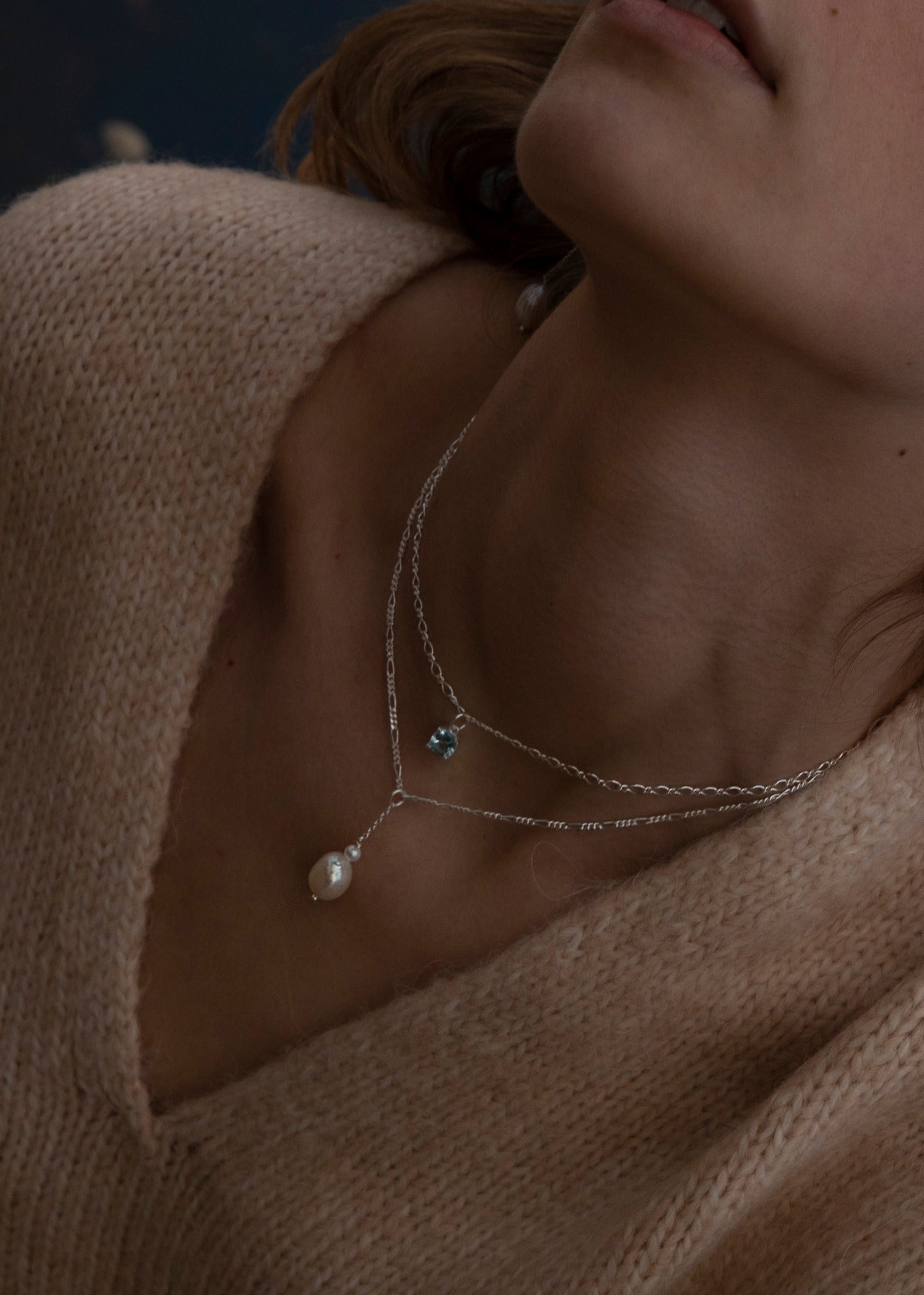 Woman with sterling silver necklaces and a blue topaz pendant and a white freshwater pearl pendant