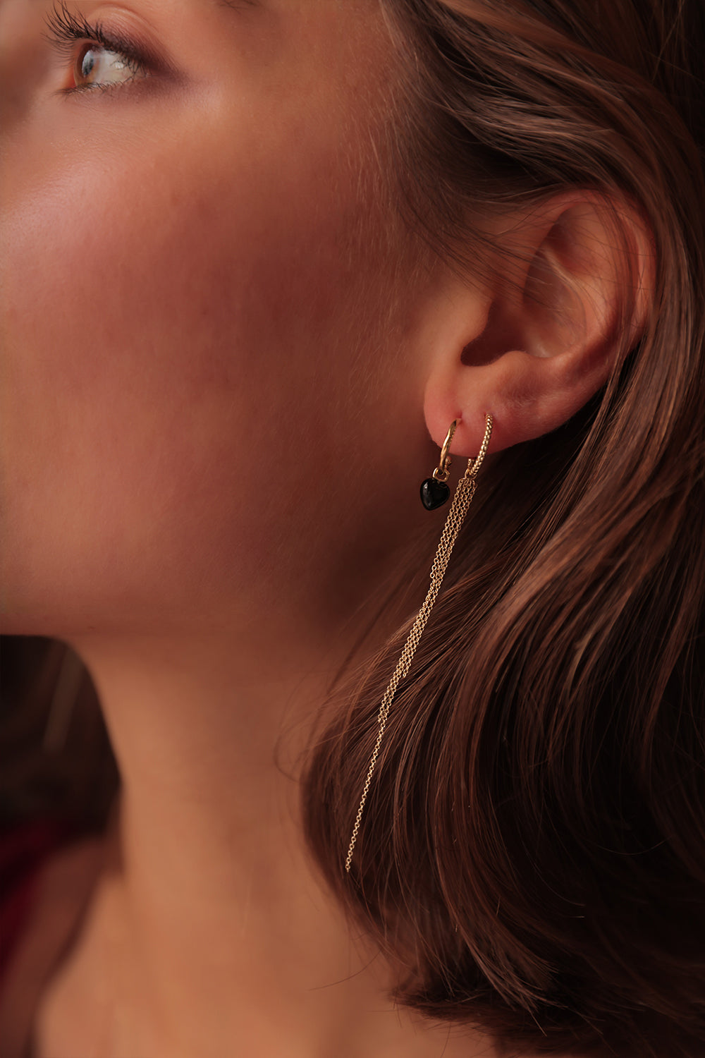 Woman wearing solid gold earrings from Carré with a heart-shaped charm for hoops and bracelets set with Black Agate