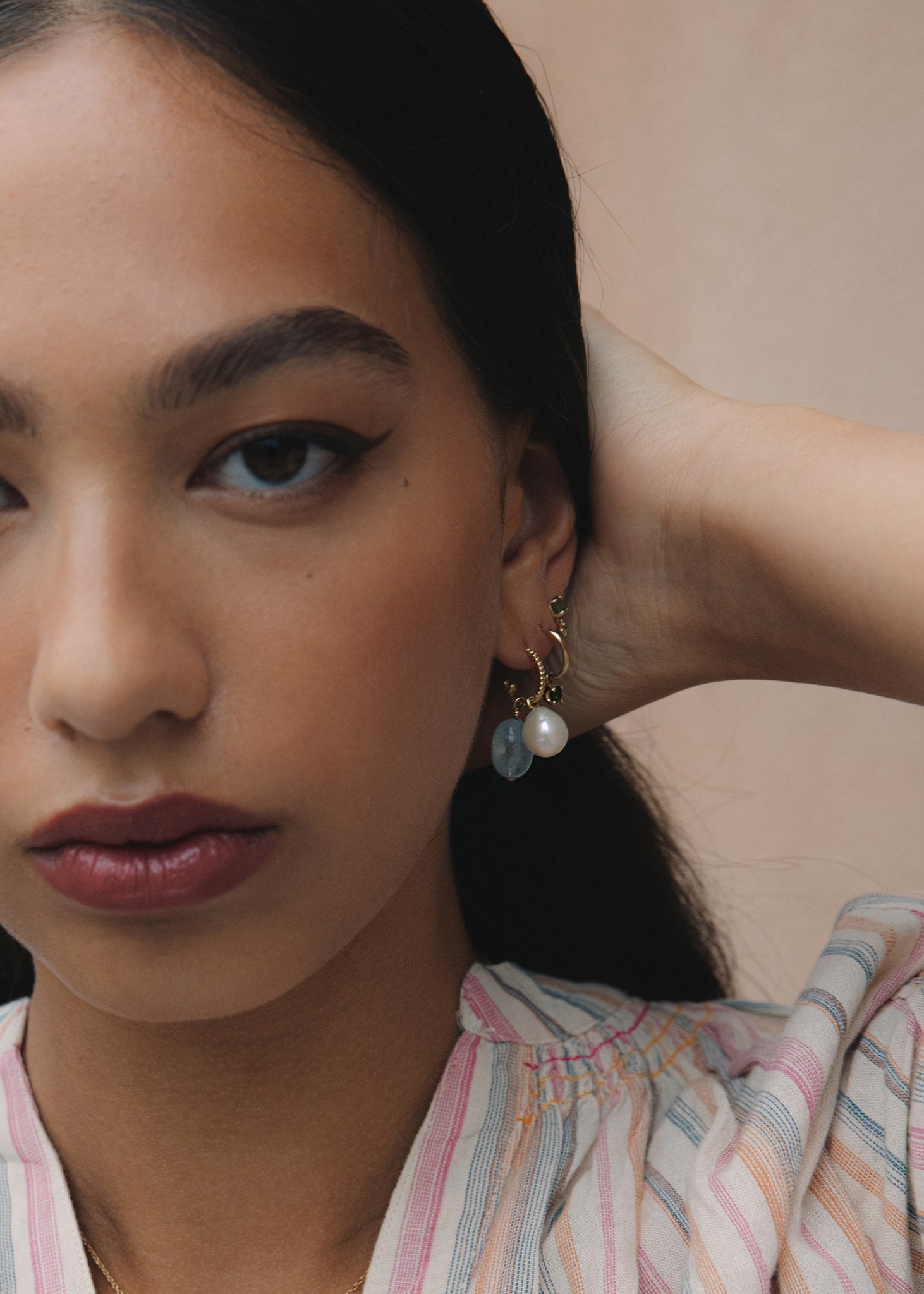 Woman wearing 10-karat solid gold charms for hoops from Carré Jewellery set with white freshwater pearl, aquamarine and green tourmaline gemstones