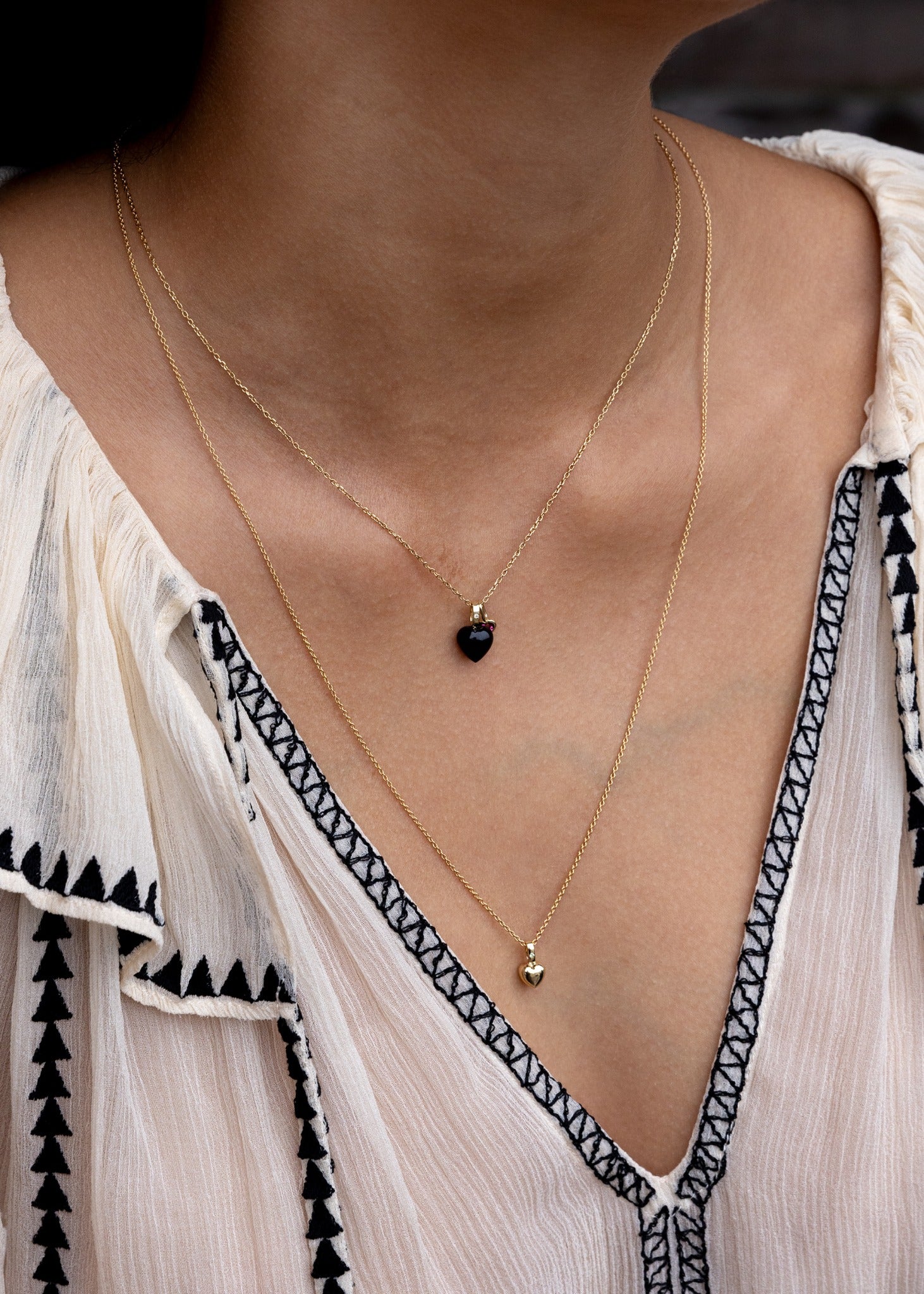 Woman wearing three heart pendants for necklaces in solid gold set with real diamonds and birthstones