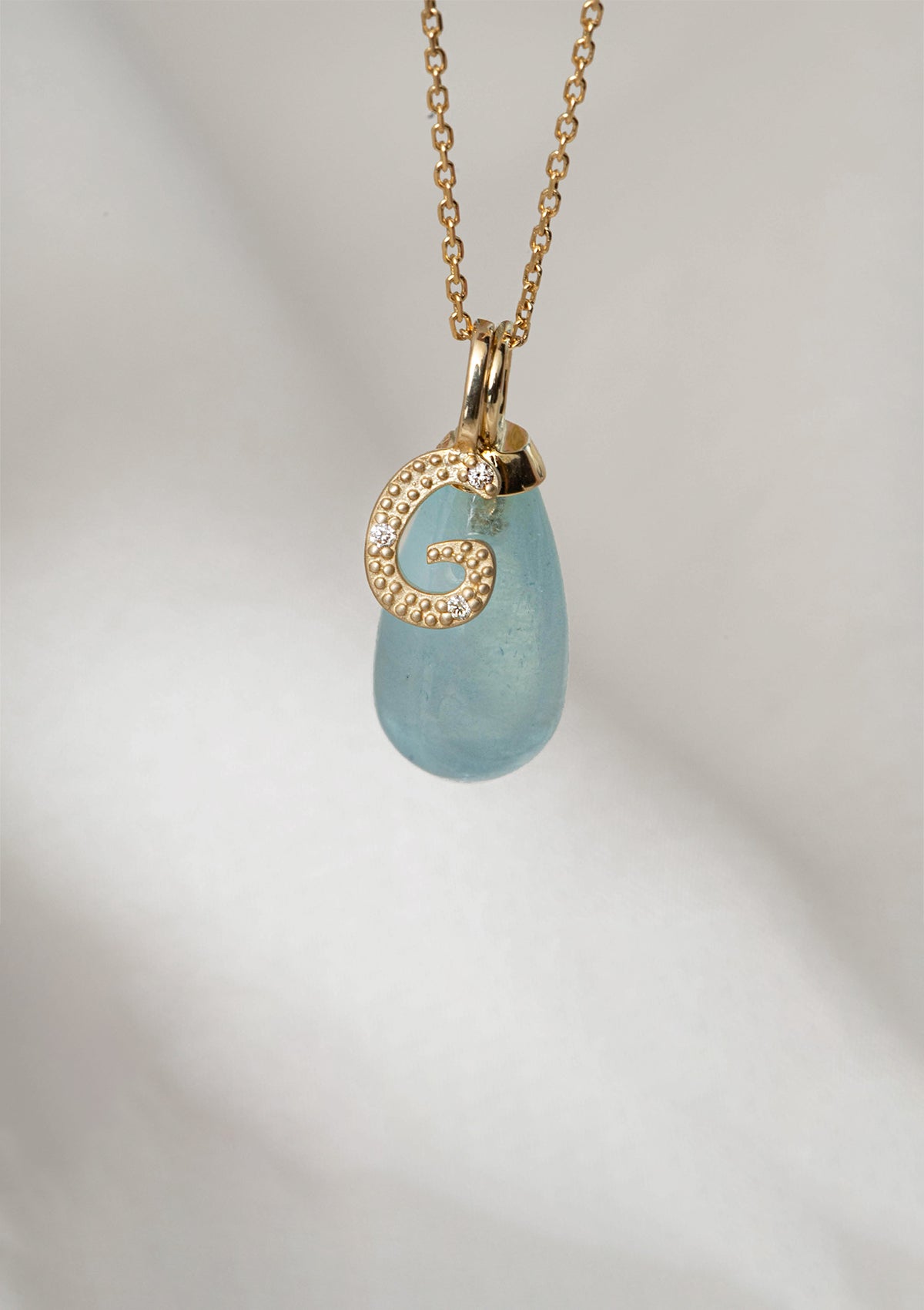 solid gold necklace with pendants from carré. The pendants are a blue aquamarine pendant and a letter pendant with diamonds in the letter G