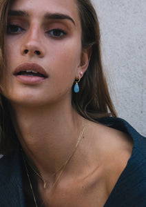 woman with gold jewellery from carré. She is wearing a letter pendant with diamond and the letter H and aquamarine earrings.