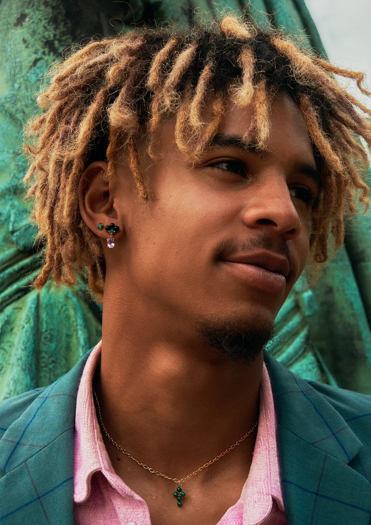 a young man wearing gold plated jewellery from carré. the gemstones in the earrings are amethyst, green agate and black agate