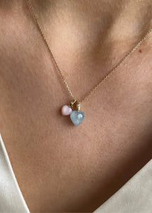 Woman with two heart shaped pendants for necklaces. One pink opal pendant and one with blue aquamarine in a heart with diamonds