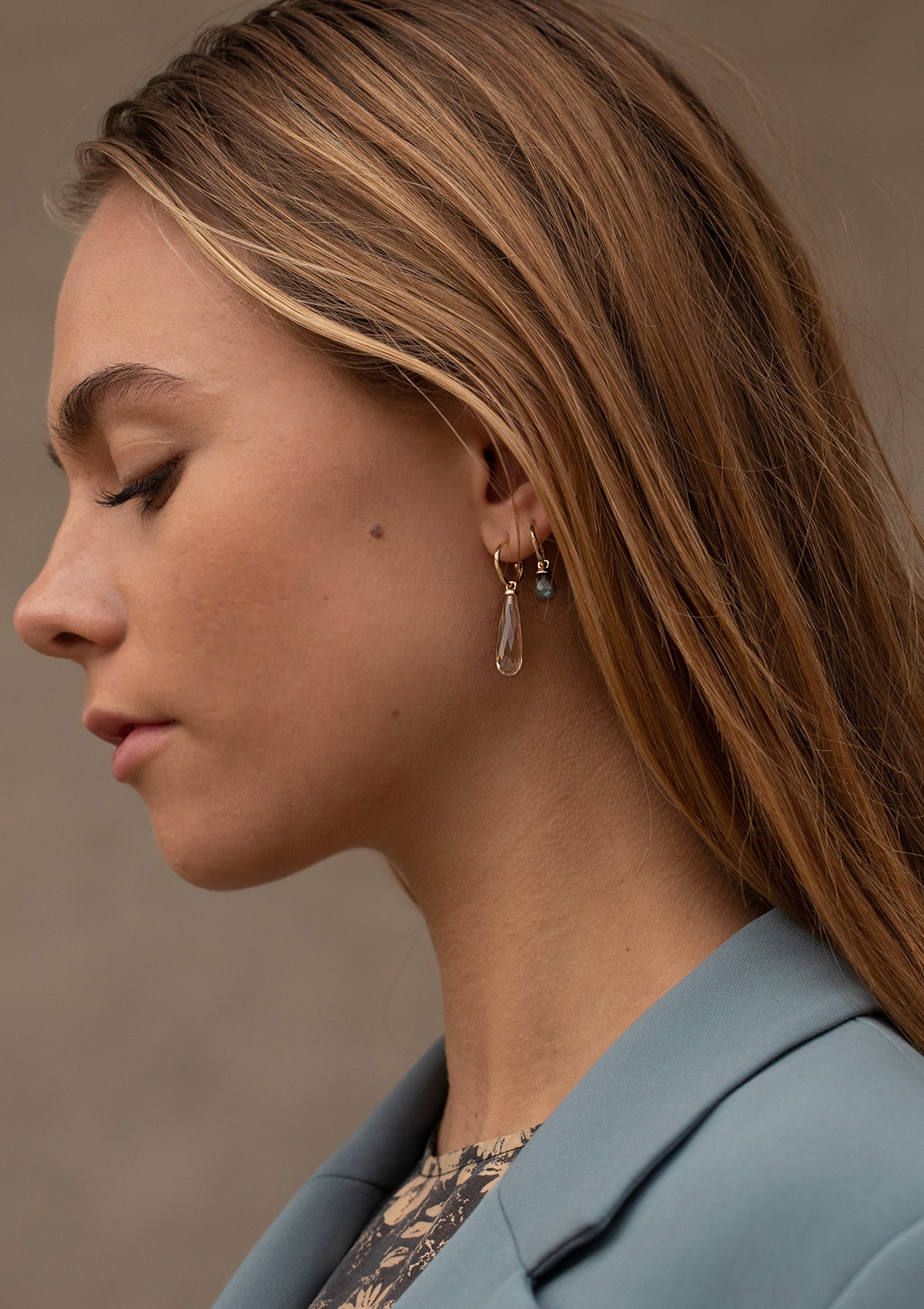 Woman wearing gold jewellery from carré. She is wearing gold hoops with long gemstone charms. The gemstones are citrine and labradorite