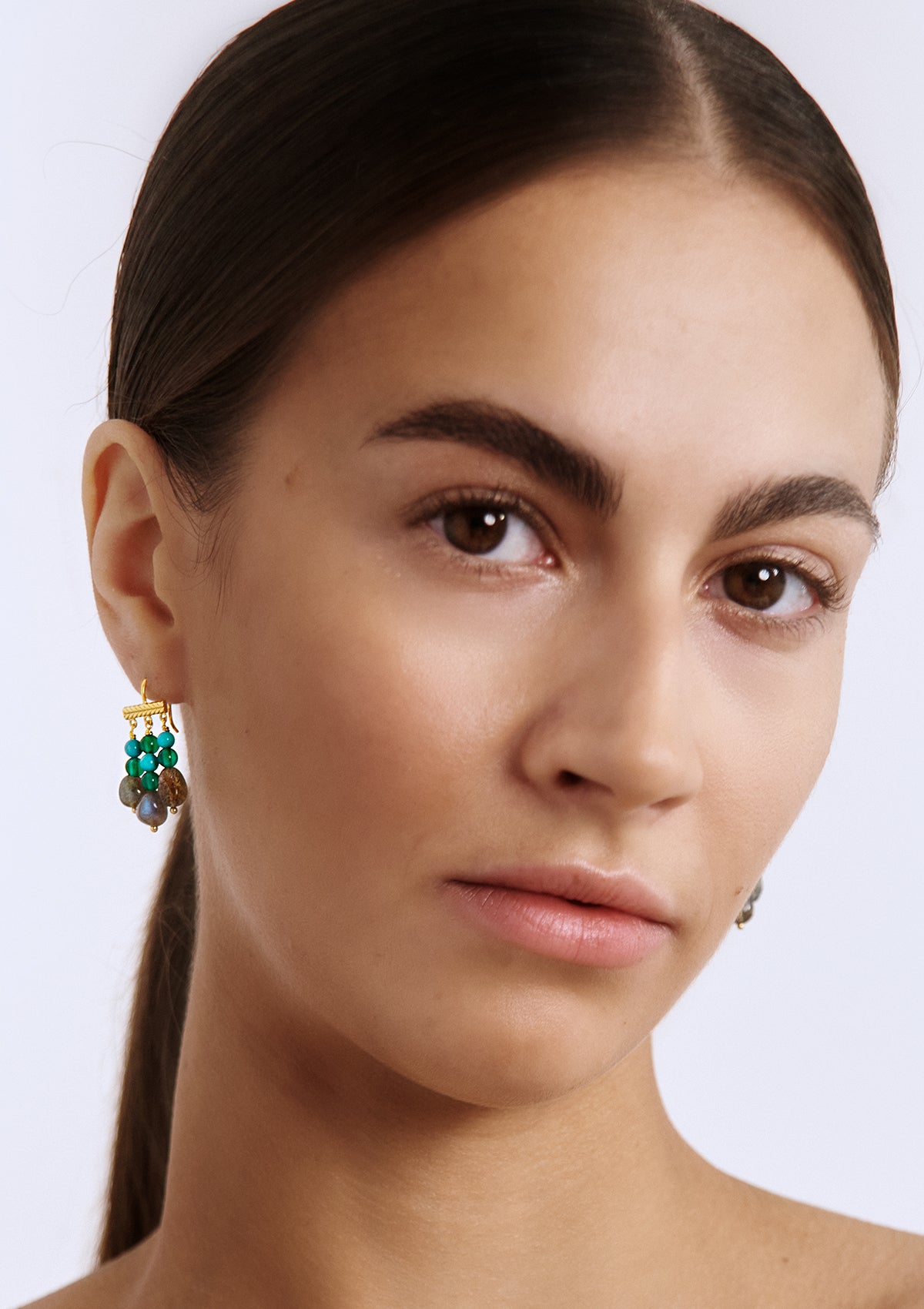 woman with large gold plated earrings with colourful gemstones from Carré. The gemstones are turqouise, labradorite and green agate