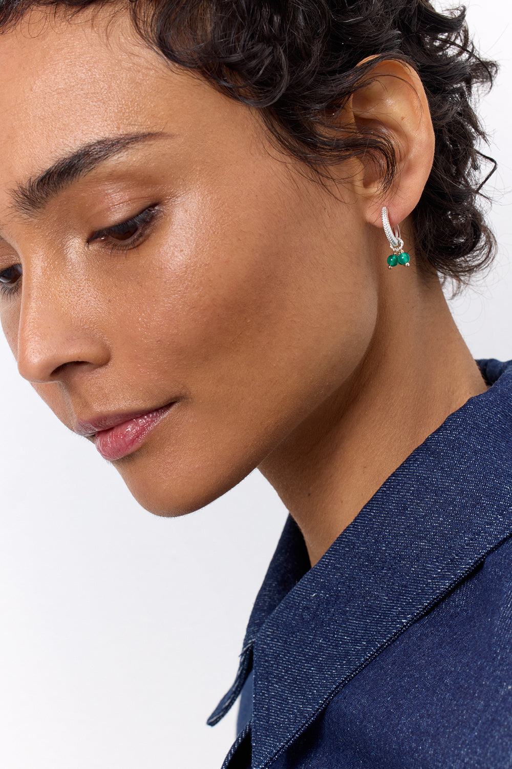 A woman wearing a sterling silver hoop with a fishbone pattern, and a charm with green agate gemstones.