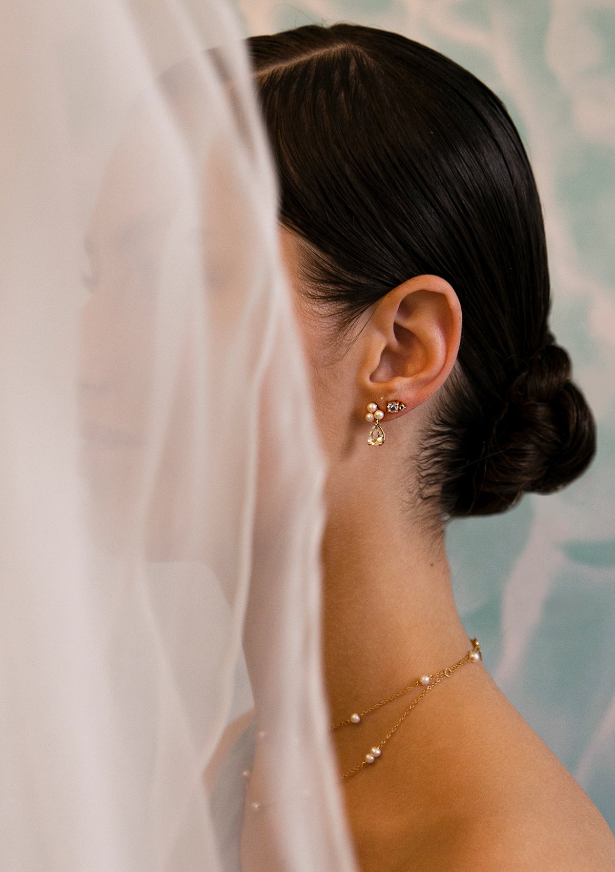 woman with long pearl earrings a prasiolite gemstone and a small earring with white topaz and blue topaz.