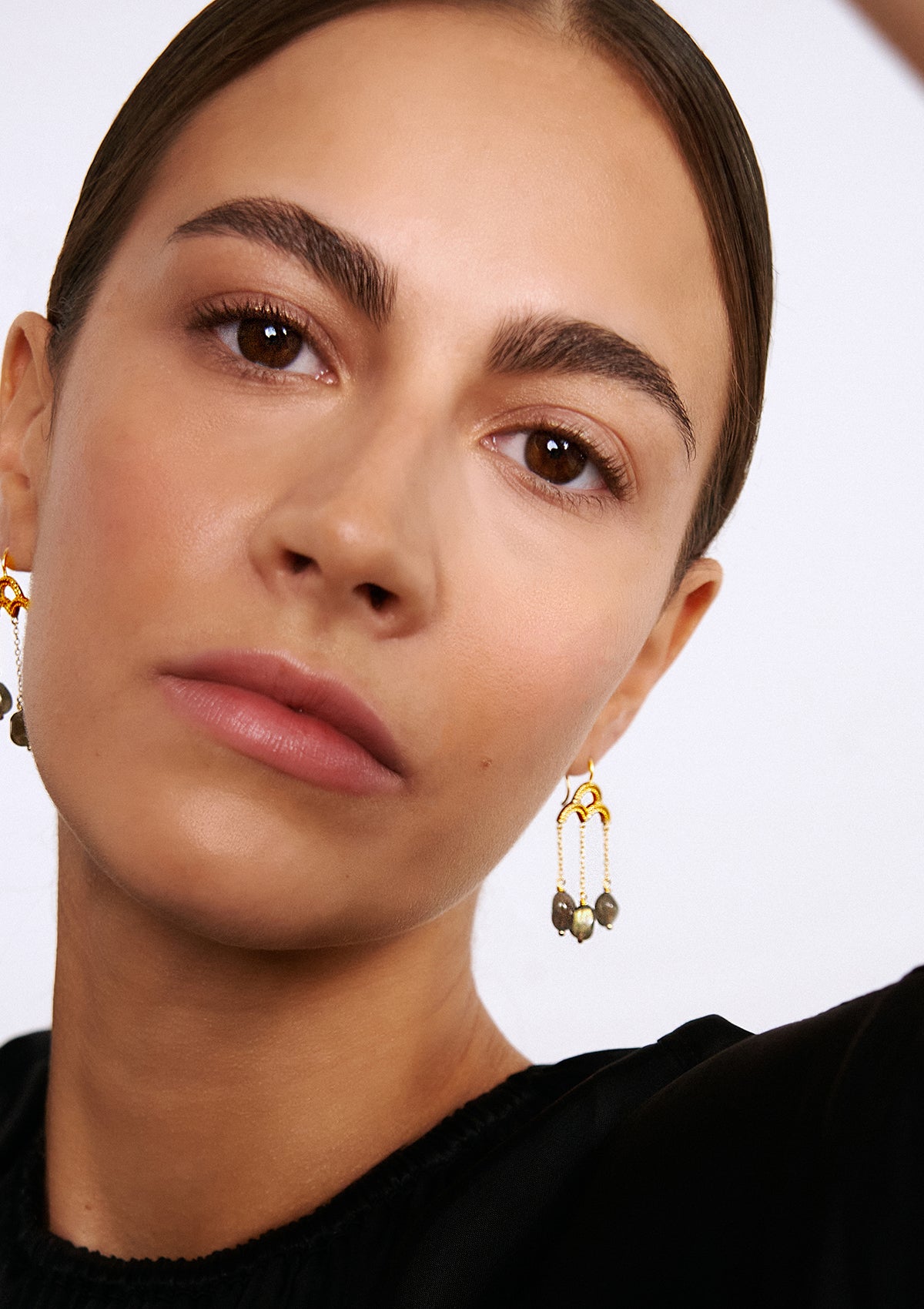 woman wearing long gold plated earrings with chains and stones from carré. The stones are labradorite gemstones