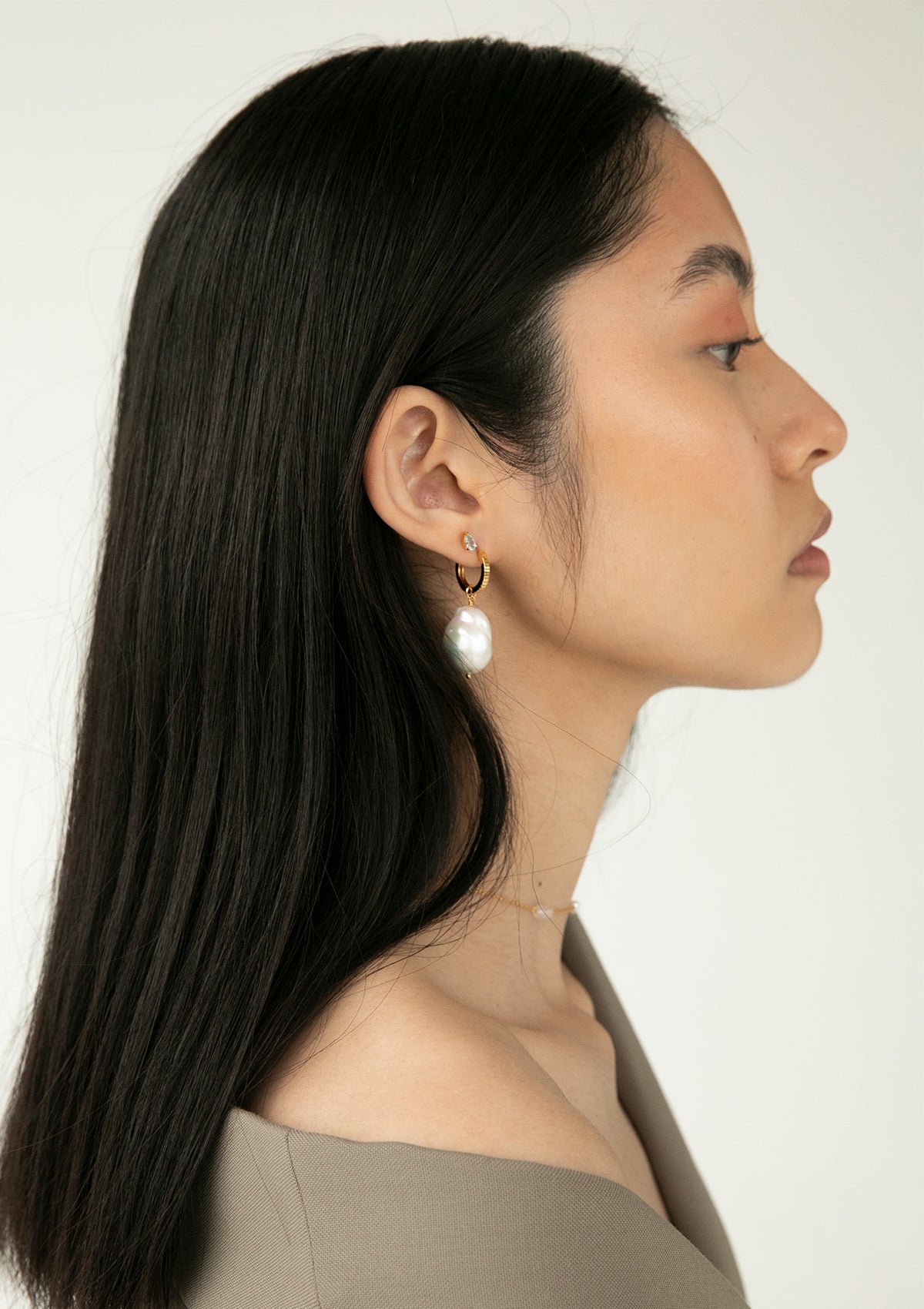 Woman wearing gold plated earrings from carré. The woman wears a twist hoop with a large baroque pearl charm for earrings.