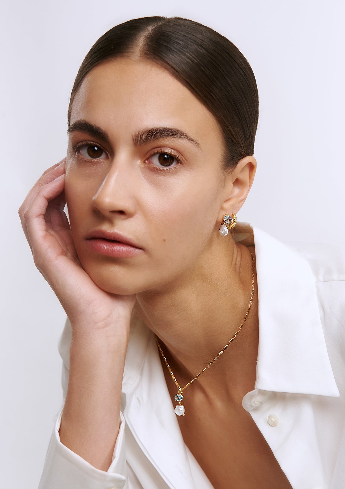 woman wearing gold plated jewellery from carré. She wears a figaro chain, a necklace pendant with pearl and blue topaz, and matching earrings with pearl and blue topaz