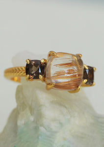 A gold plated ring with three gemstones from carré. The big gemstone in the middle is a golden rutile quartz, and the two on the sides are smokey quartz