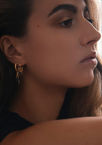 Woman with gold plated boheme style jewellery from carré. The long earrings are hoops with a smokey quartz charm and an earring with smokey quartz and golden rutile quartz