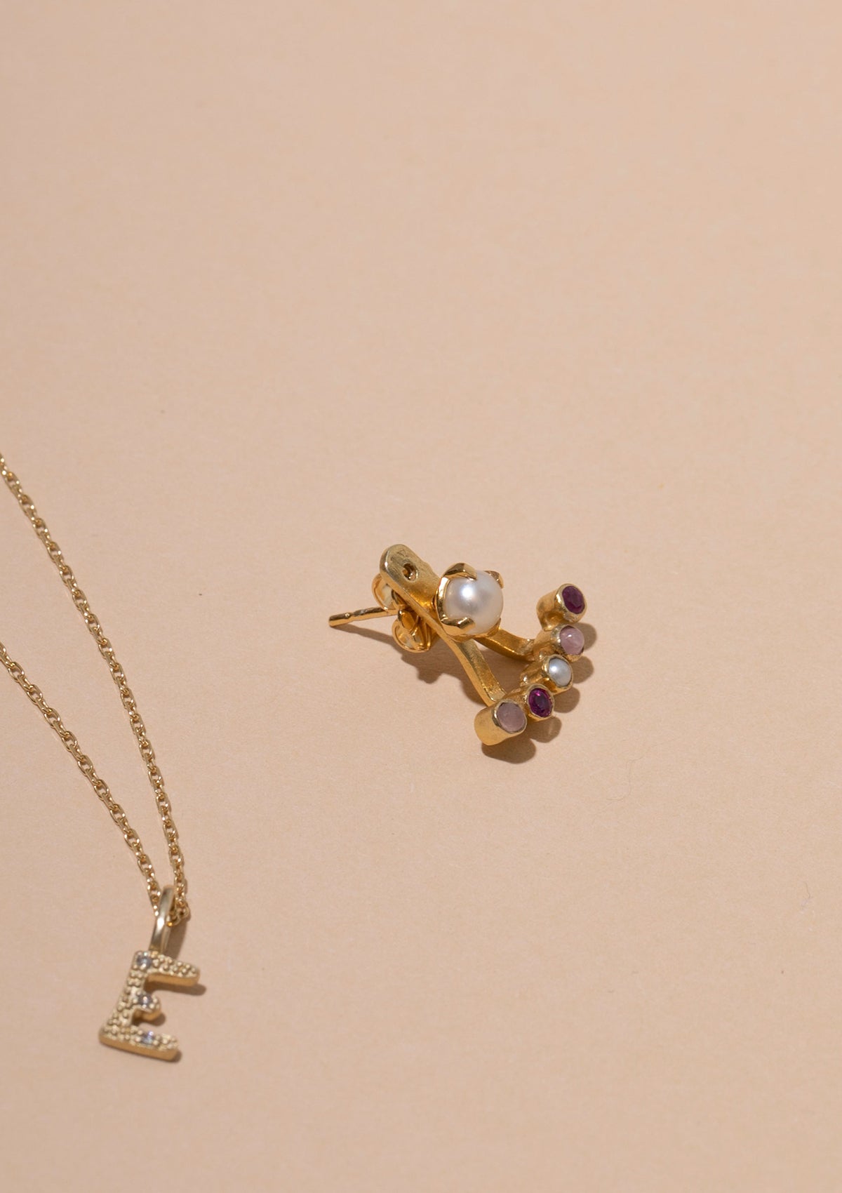 gold jewellery with stones from carré. A diamond pendant for necklaces with the letter E and an earring with pearl and ruby