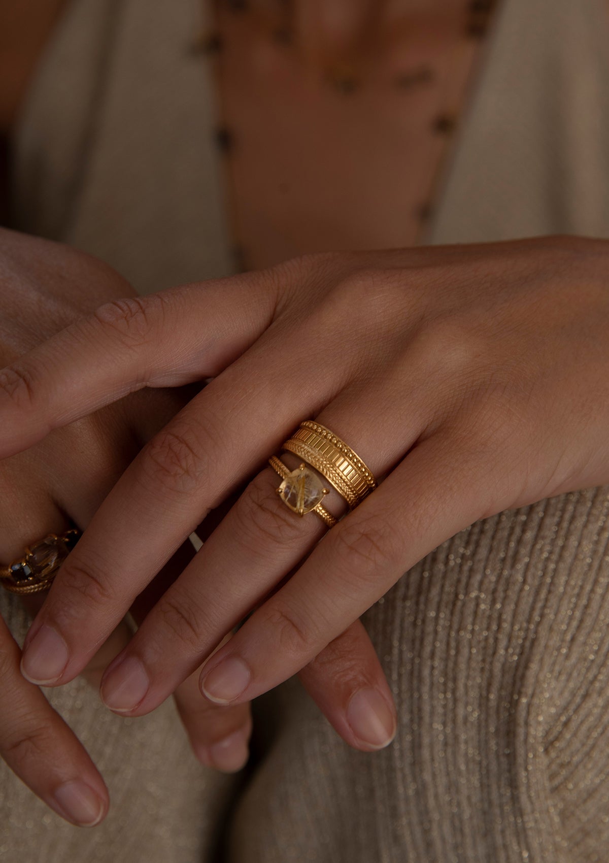 Woman with gold plated rings from carré. One ring is a large stone ring with golden rutile quartz, and the other is a ring with a broad band.