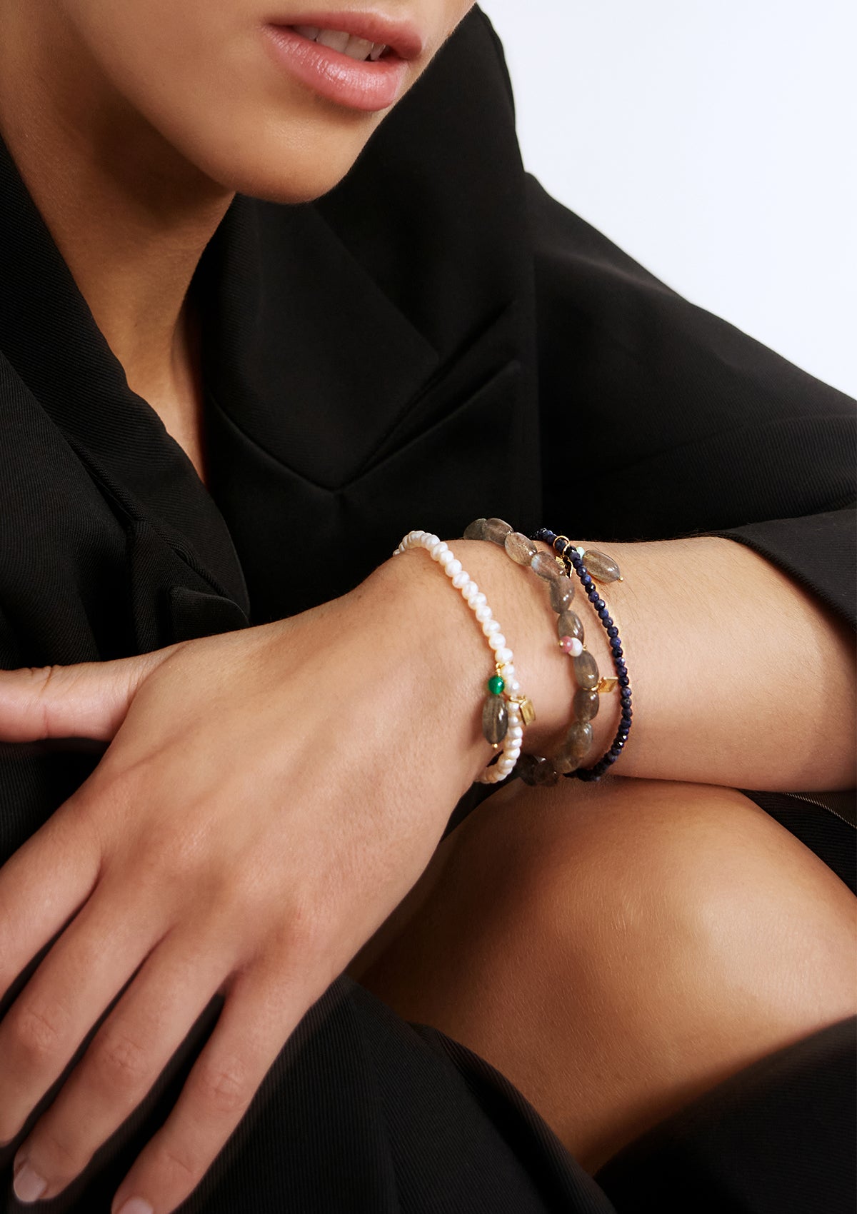 Kvinde med tre guldbelagte armbånd med store ædelsten fra carré. Armbåndene er med safir, labradorit og perlearmbånd.