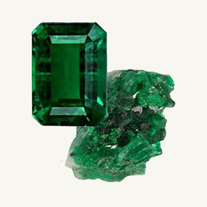 A facet-cut emerald and a raw emerald gemstone on a beige background