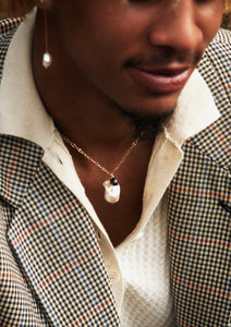 a young man with a large freshwater pearl pendant and a pendant with a black agate gemstone as well as a long pearl earring