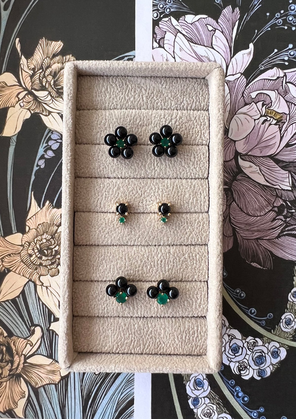 Three floral shaped earrings with black agate stones and green agate from carré in a beige jewellery box.