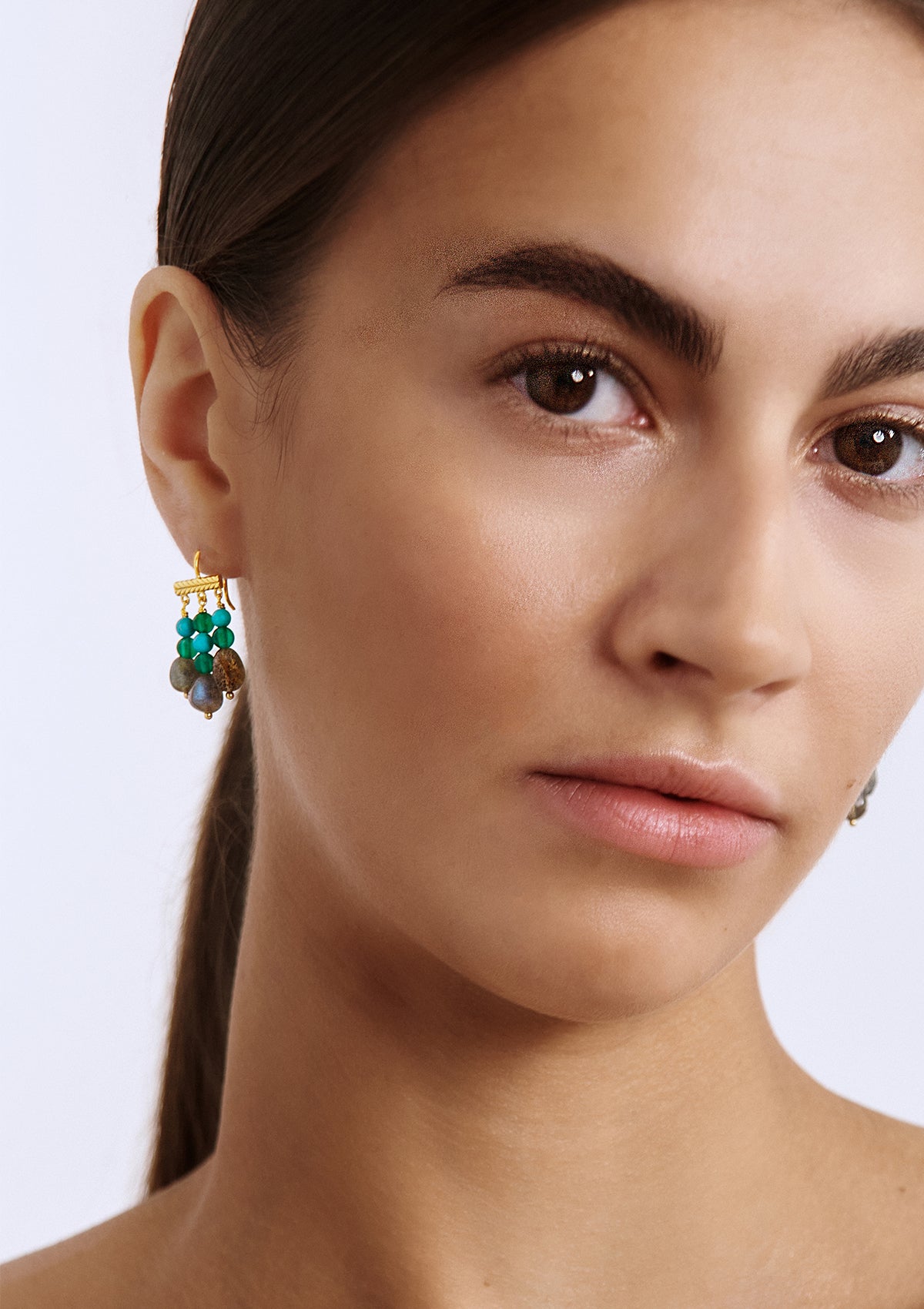 a woman with large and long gold plated earrings with gemstones from carré. The gemstones are turquoise, green agate and labradorite gemstones