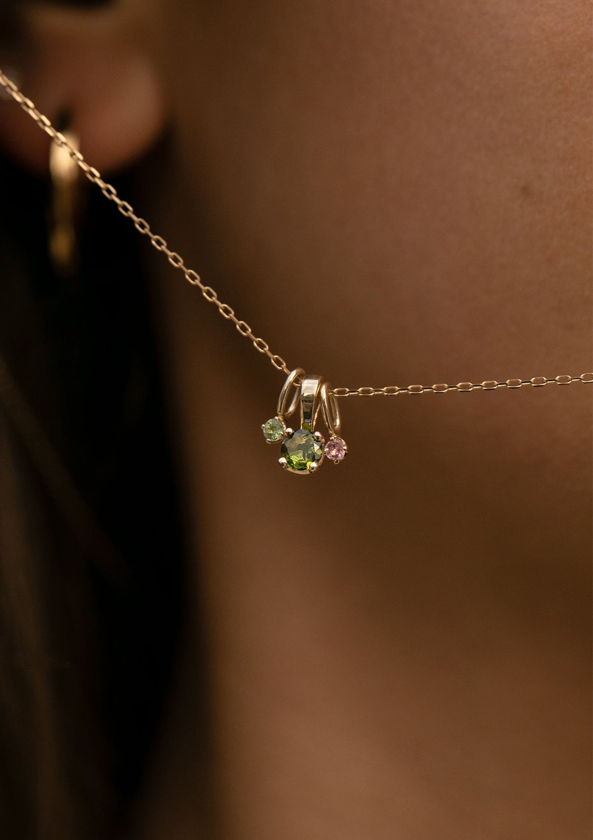 woman holding a necklaces with three tourmaline pendants in solid gold with green and pink tourmalines