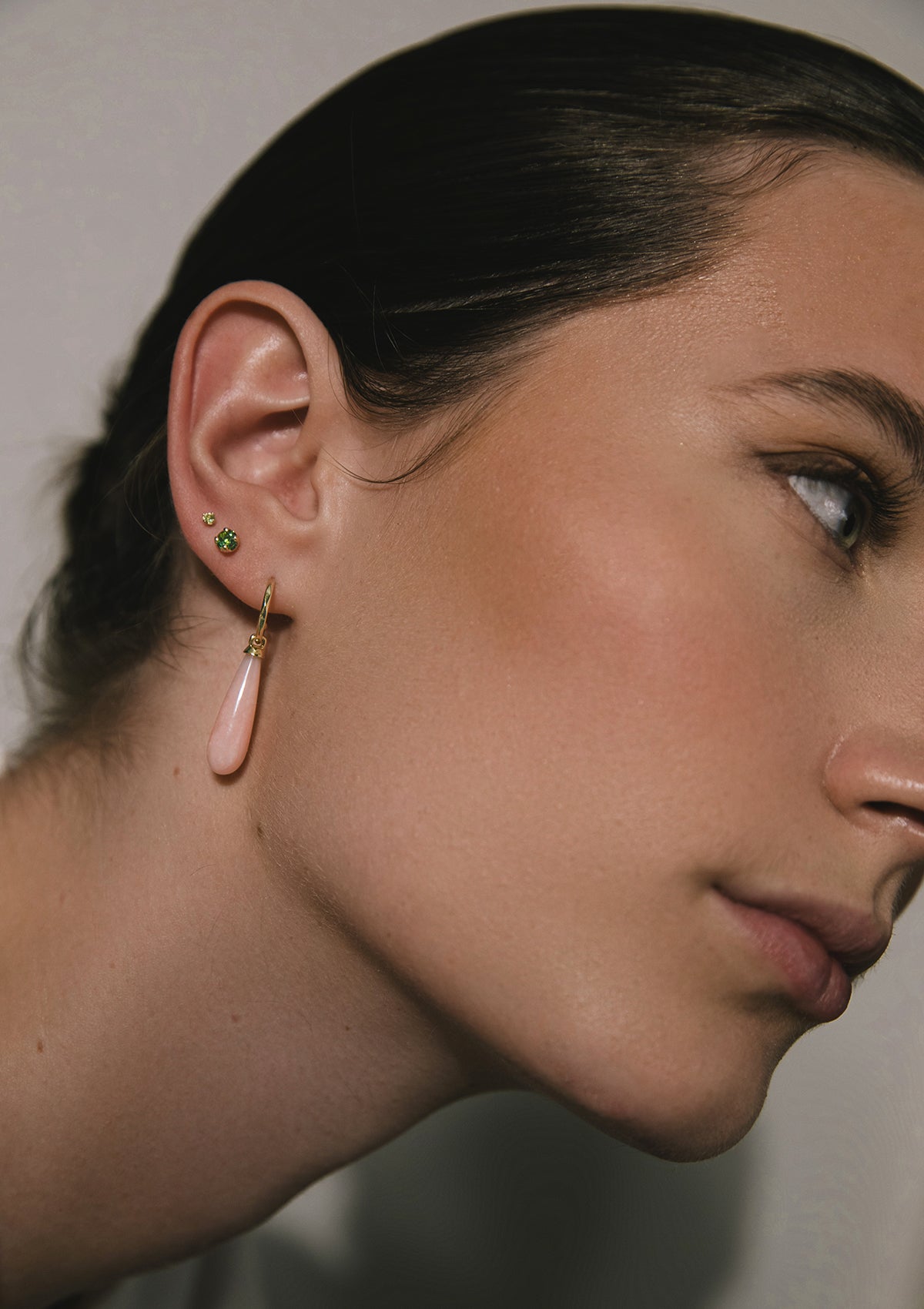 woman with solid gold jewellery from carré. She wears a long earring with a pink pendant and two ear studs with green tourmaline